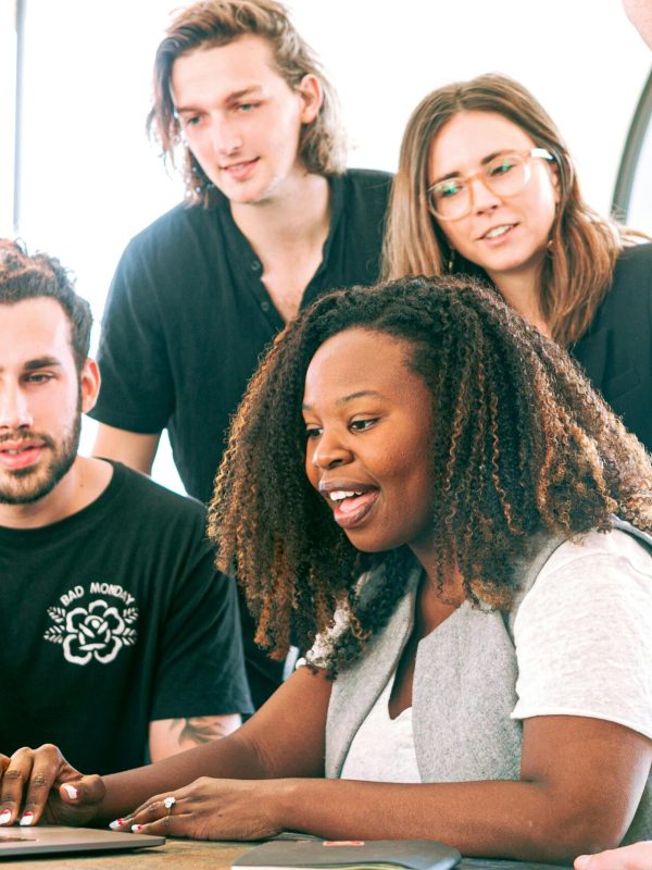 A diverse group of young professionals collaborating around a laptop in a modern office setting. Perfect for business or tech concepts.