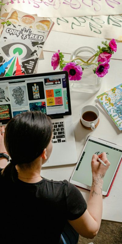 Artistic workspace featuring calligraphy and digital design on a tablet and laptop.