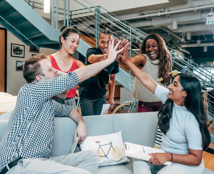 A multicultural office team high-fiving and celebrating a successful collaboration.
